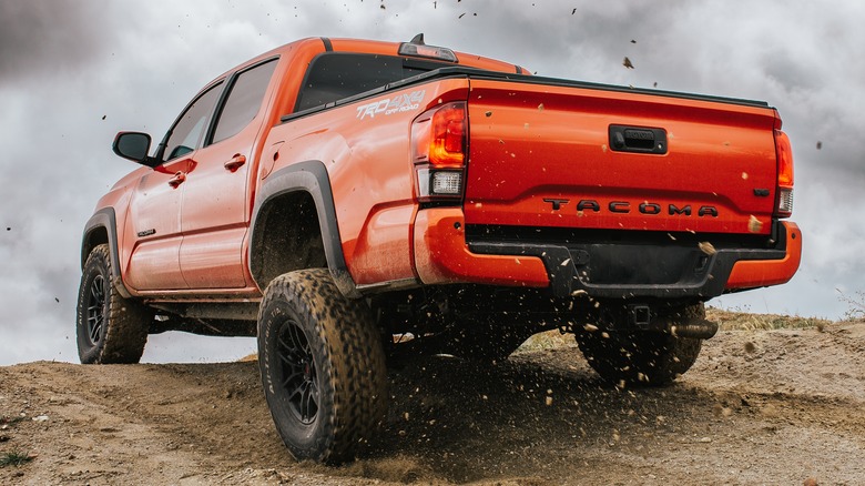 An orange Toyota Tacoma TRD driving through dirt and sand, mud flying up, with gray skies in the background.