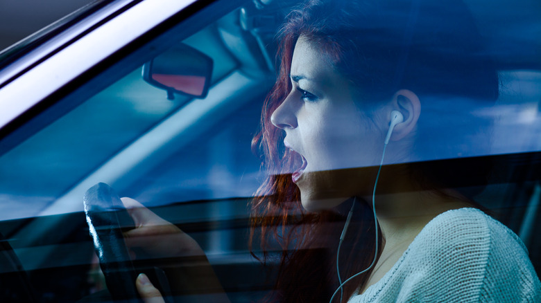 A woman singing while driving with earphones in