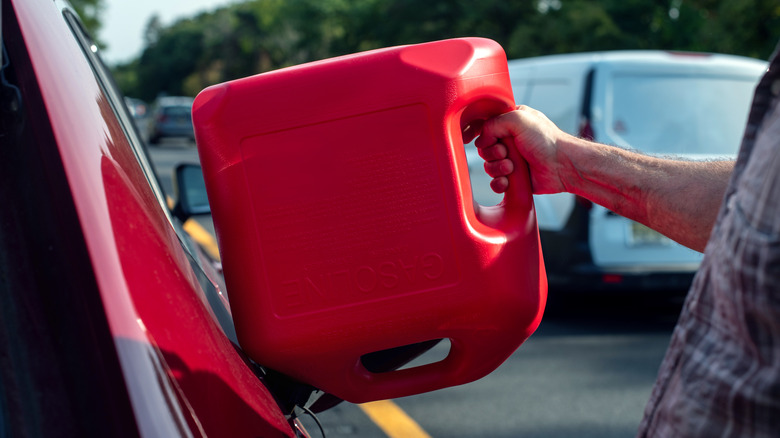 A person pouring gas from a can into a car's tank