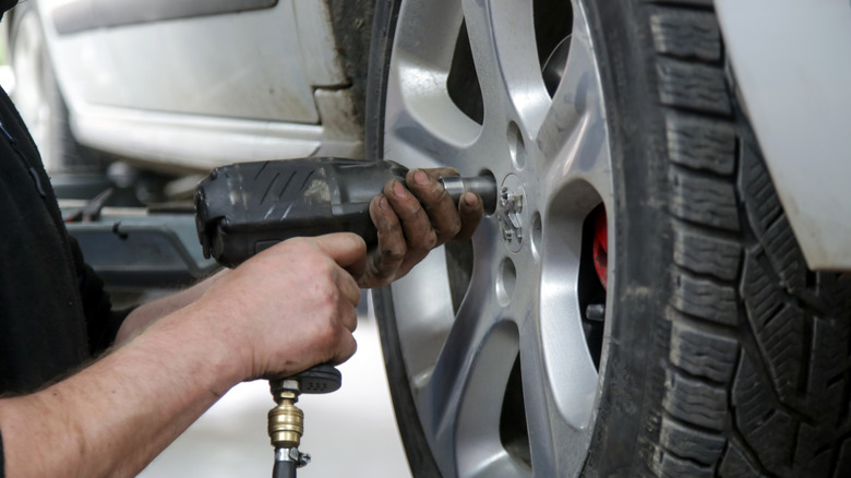 A mechanic tightens the lug nuts on a passenger car tire.