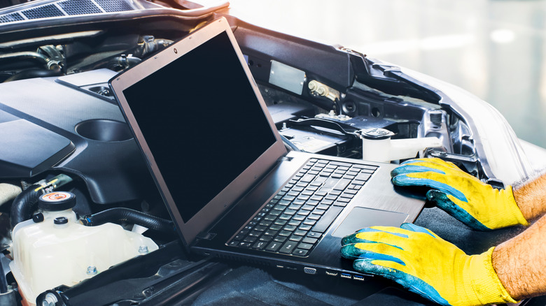 A technician using a laptop placed on a car's engine bay.