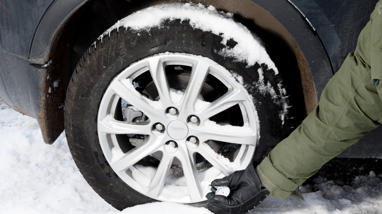 A car owner checking the tire pressure using a handheld gauge while the vehicle is parked in snow
