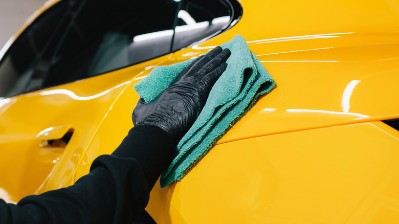 Detailer using a microfiber cloth on a yellow sports car.
