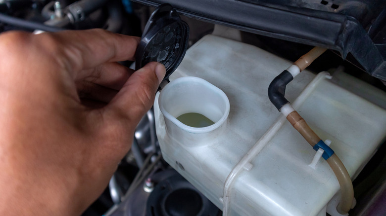 A hand holding the cap to a windshield wiper fluid reservoir.