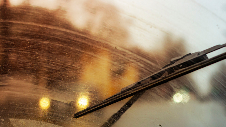 A dirty, filmy windshield with a wiper blade trying to clean it.