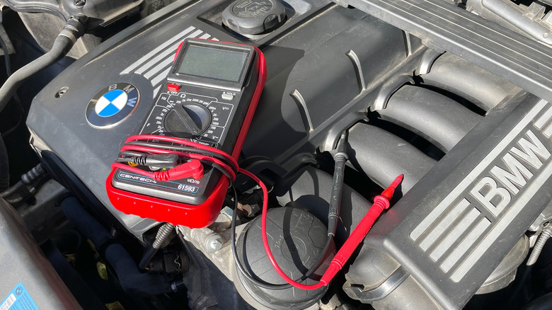 A multimeter sitting on top of a BMW engine, ready to diagnose an electrical issue.