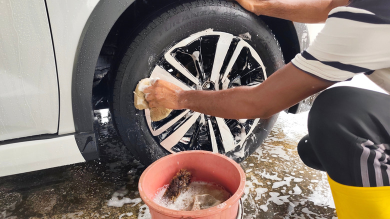 Man washing car tire with sponge and soapy water