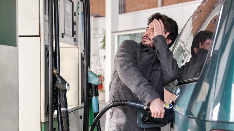 A person staring at fuel pump looking worried about gas prices as they fill up their tank
