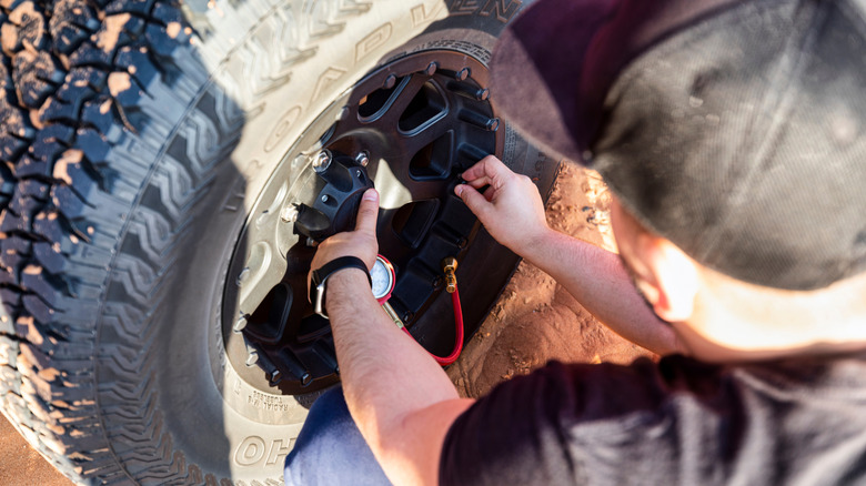 Guy in black shirt and black hat airing down black off road tire