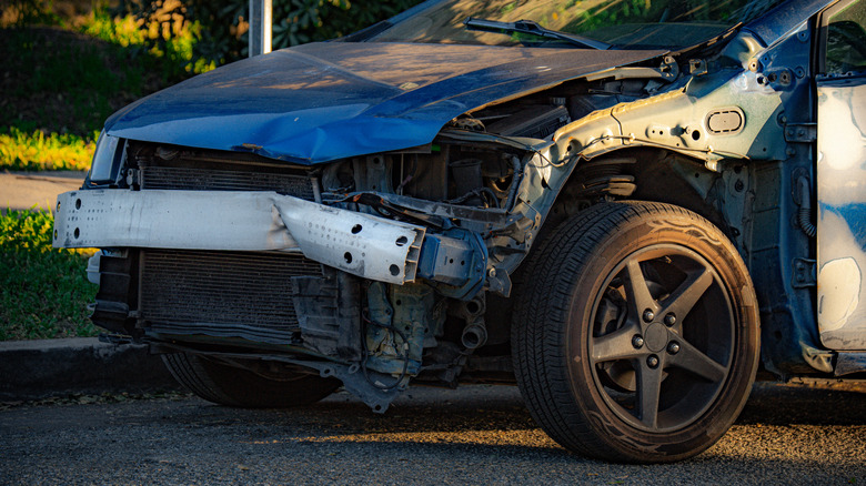 A severely damaged car sits on the side of the road.