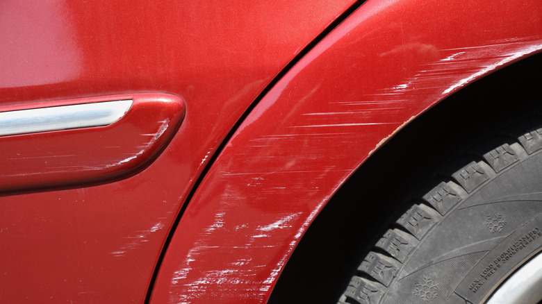 A red car with scratches on its fender