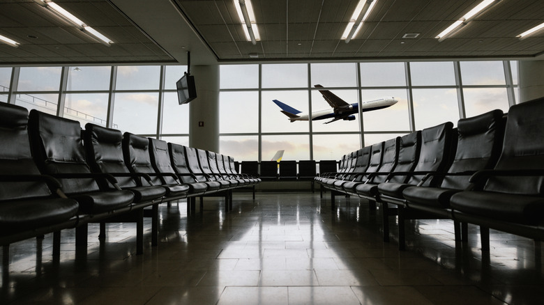 A dystopian empty airport seating area with no one waiting for a flight, with a plane taking off in the background.