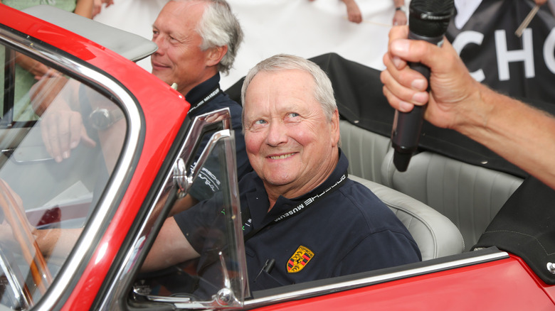 Wolfgang Porsche sits in a red convertible while being interviewed