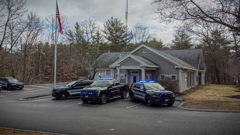 Three police cars with flashing lights parked in front of the Stow, Massachusetts police department