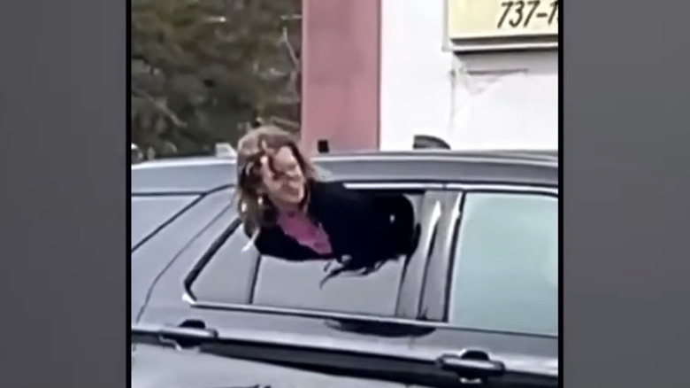 A woman squeezes out the half-open window of a police car to escape custody