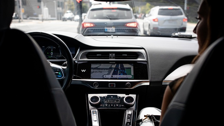 A driverless Waymo robotaxi with a passenger driving in traffic.