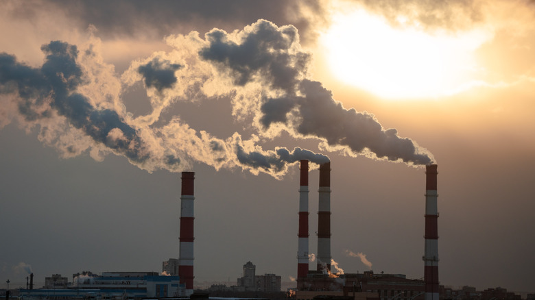 Smokestacks from a fossil fuel plant underneath a Sun looking to replace it