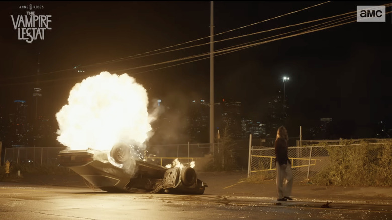 Sam Reid as The Vampire Lestat walks away from a flipped over burning Camaro in the middle of the street