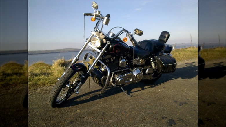 A Harley Davidson Wideglide sits near water.