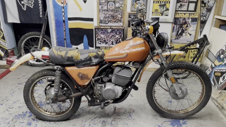 A Harley-Davidson SX250 sits in a shop with various hockey posters and memorabilia in the background.