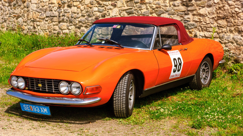 An orange Fiat Dino parked near a stone wall