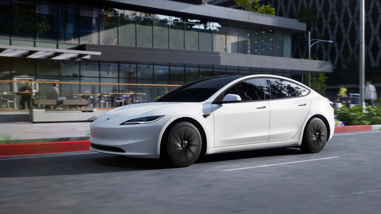 A white Tesla Model 3 parked on city street near modern-looking buildings
