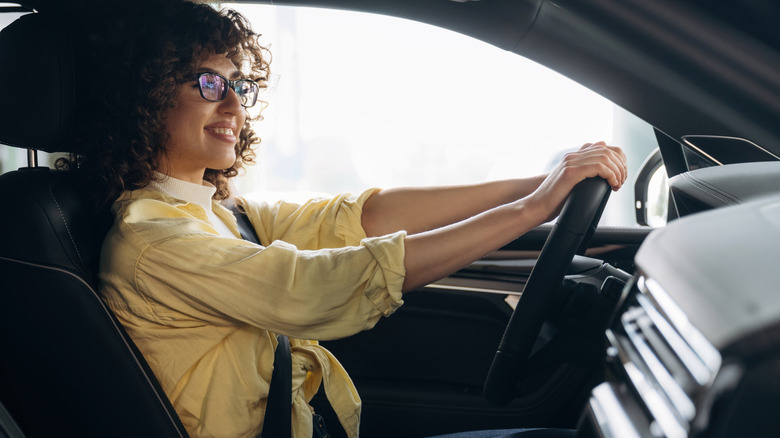 A woman with curly hair drives with both hands on the wheel.