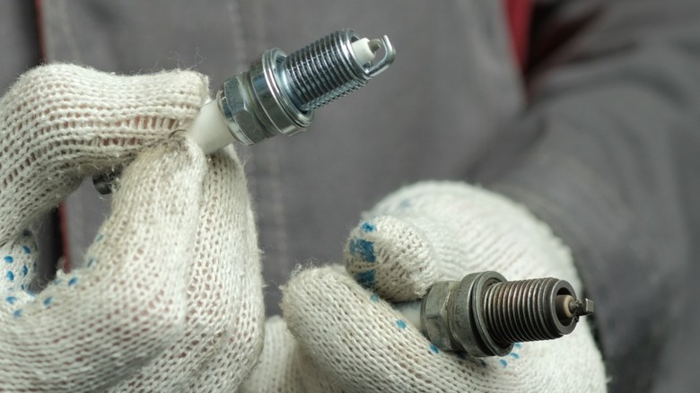 Gloved hands holding one good spark plug, one defective spark plug