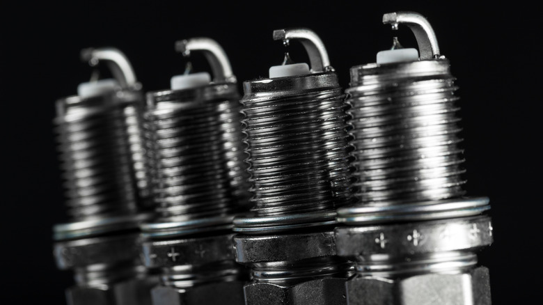 A set of four new spark plugs amidst a dark background