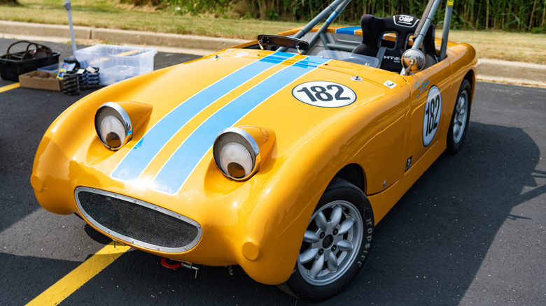 A modified Austin Healey Sprite, yellow with blue stripes and googly "eyeballs," parked in the sun