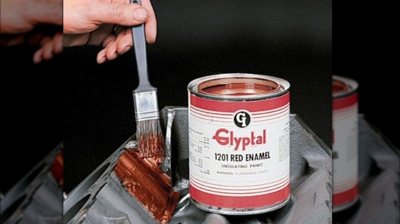 A person applying red Glyptal paint to the inside of a engine's lifter valley.