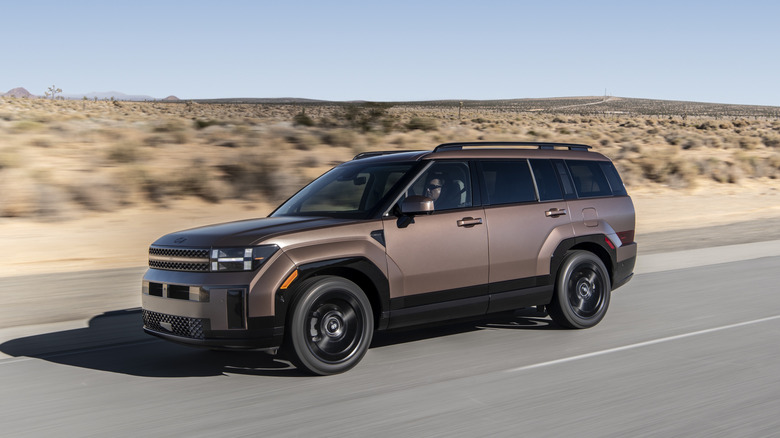 A side profile of a bronze 2026 Hyundai Santa Fe Hybrid on a roadway.