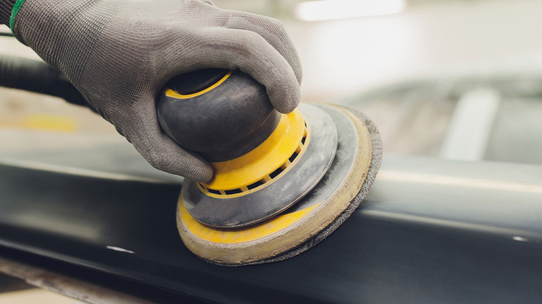 Man holding a sanding tool to smoothen a car part before painting