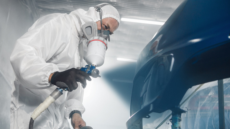 A professional car painter applying color to the disassembled bumper of a car