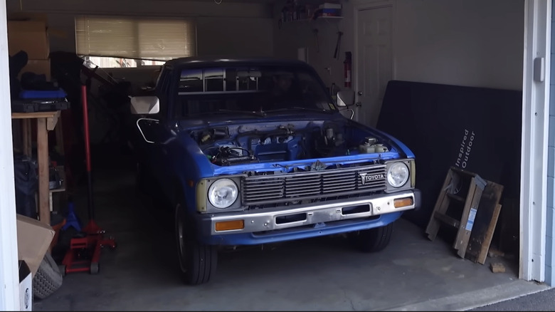 Front 3/4 view of a blue 1982 Toyota Pickup converted into an electric vehicle pulling out of a garage