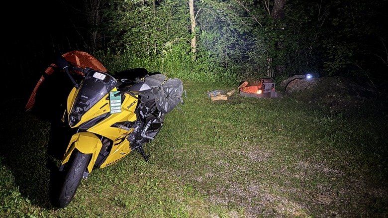 Amber's yellow motorcycle ahead of her orange tent and a campfire, in the dark