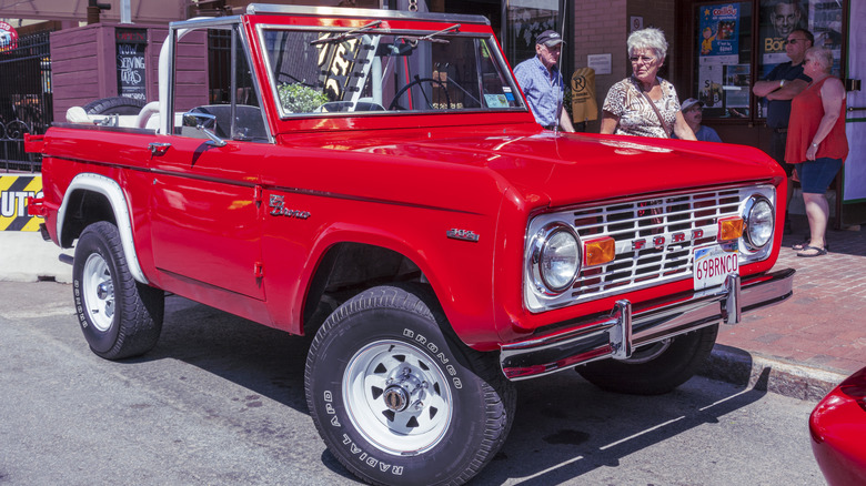 Front 3/4 view of a red first-gen Ford Bronco parked on the street.