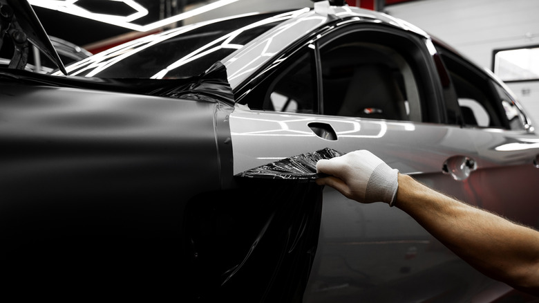Technician installing a matte black vinyl wrap on a gray car