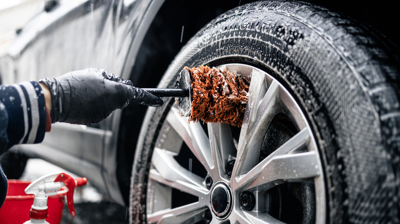 Man cleaning the front wheel of a car with a brush and soapy water