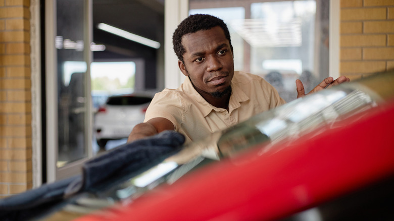 A young man wiping the windshield of a car with a towel