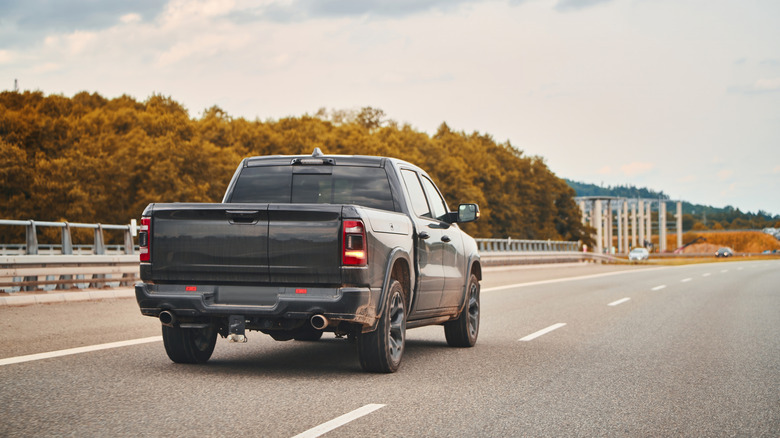 A rear-end view of a black pickup truck driving on the left-most lane on an empty highway.
