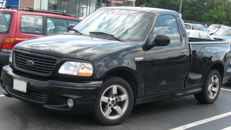 A black Ford F-150 SVT Lightning parked on a paved surface with other cars in the background