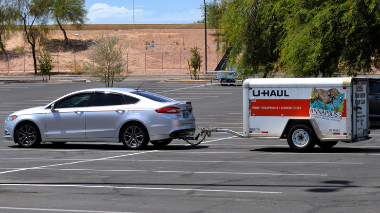 A Silver Ford Fusion towing a U-Haul trailer.