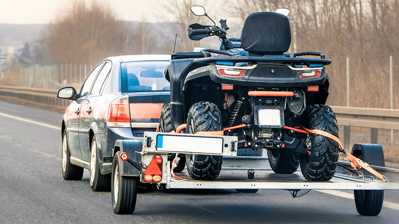 A black sedan towing an ATV on a trailer.