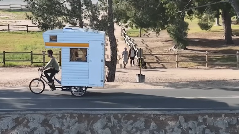 One of the Dangie Bros riding a bike camper near some people walking on a sidewalk