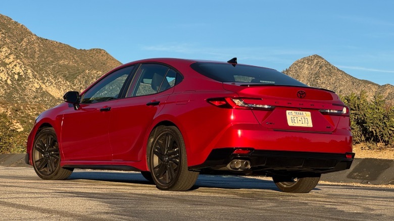 A rear three-quarters shot of the red Camry Nightshade parked on asphalt in front of a view of mountains and a blue sky