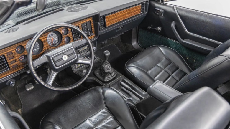 A look down at the black interior of the 83 Fox with its fake wood dash and four-spoke steering wheel