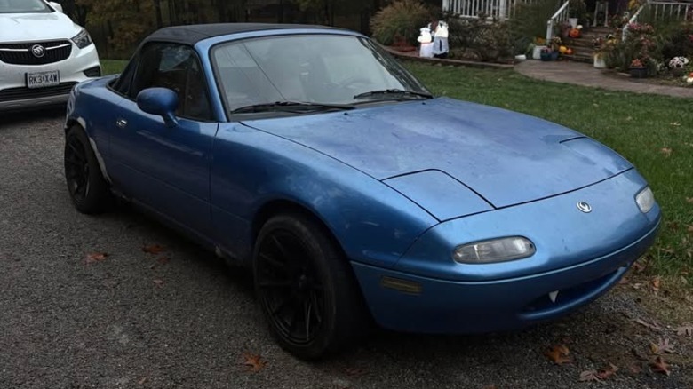 Front 3/4 view of a blue Mazda Miata with bondo around the rear fender