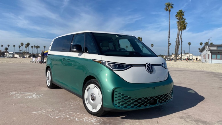 A front three quarters shot of the green and white ID Buzz parked on concrete in front of palm trees