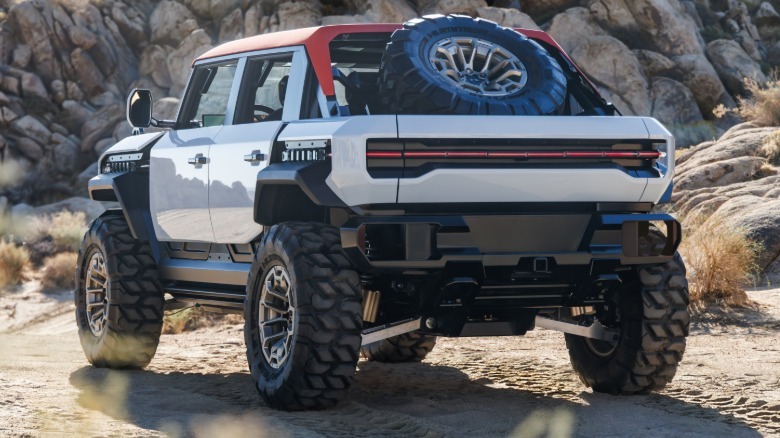 A rear three-quarters shot of the white Hummer X SUV parked on dirt in front of rocks in the desert